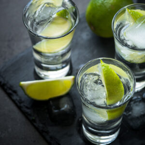 Shot glasses of blanco tequila with ice and limes.