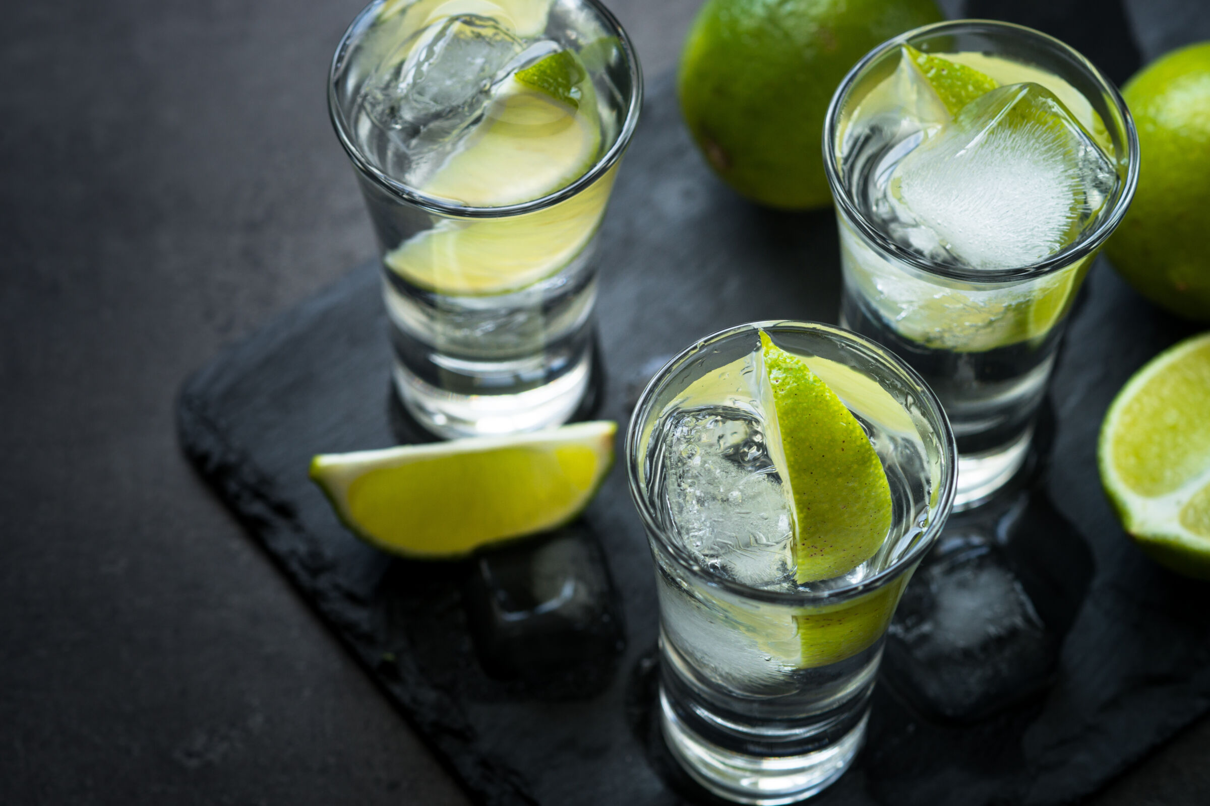 Shot glasses of blanco tequila with ice and limes.
