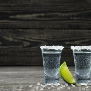 Two glasses of cold silver tequila with lime wedges.