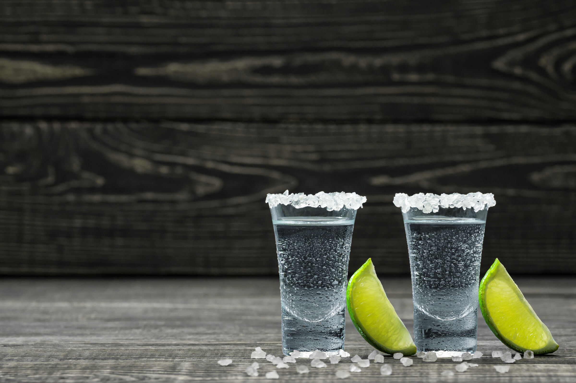 Two glasses of cold silver tequila with lime wedges.